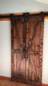 Double barn doors with British brace design and wooden frame, accented with iron clavos.